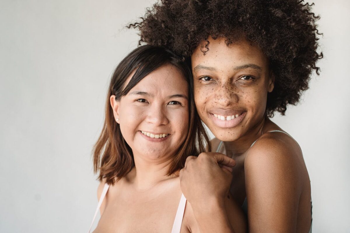 Two diverse women smiling warmly in a bright, natural light portrait, celebrating friendship and diversity.